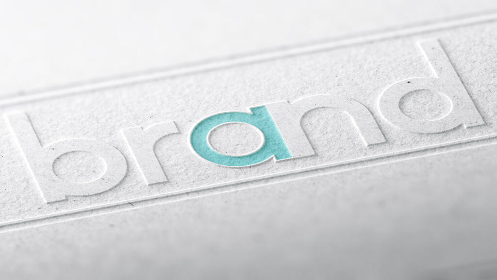 Close-up of the word 'brand' embossed on paper with the letter 'a' highlighted in light blue, emphasizing branding design.
